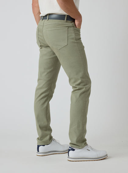 Men's Henderson 5 Pocket Pant in Moss, back model view featuring a five-pocket silhouette styled with a navy belt and white golf shoes