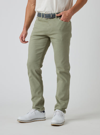 Men's Henderson 5 Pocket Pant in Moss, front model view hand it pockets  featuring a five-pocket silhouette styled with a navy belt and white golf shoes