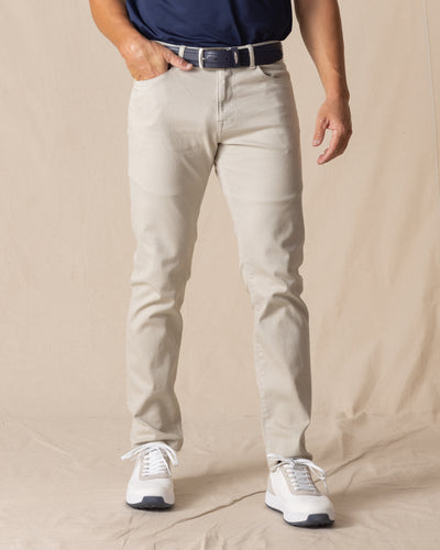 Men's Henderson 5 Pocket Pant in Stone, front model view featuring a five-pocket silhouette in a warm off-white colorway, styled with a navy belt and white shoes