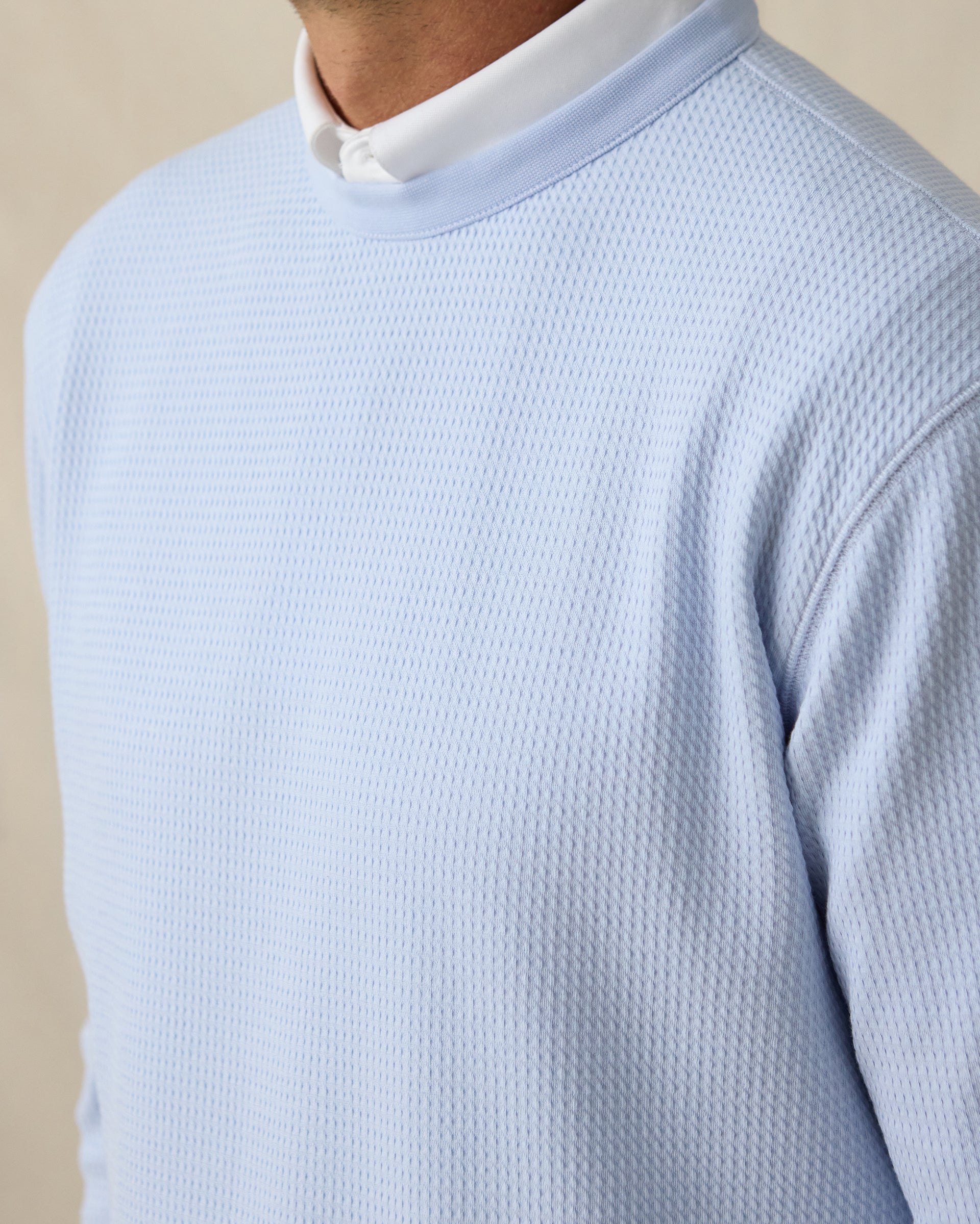 Close-up of light blue textured bubble knit fabric on men’s crewneck pullover layered over a white polo collar.