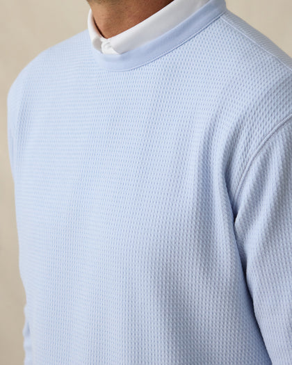 Close-up of light blue textured bubble knit fabric on men’s crewneck pullover layered over a white polo collar.