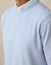 Close-up of light blue textured bubble knit fabric on men’s crewneck pullover layered over a white polo collar.