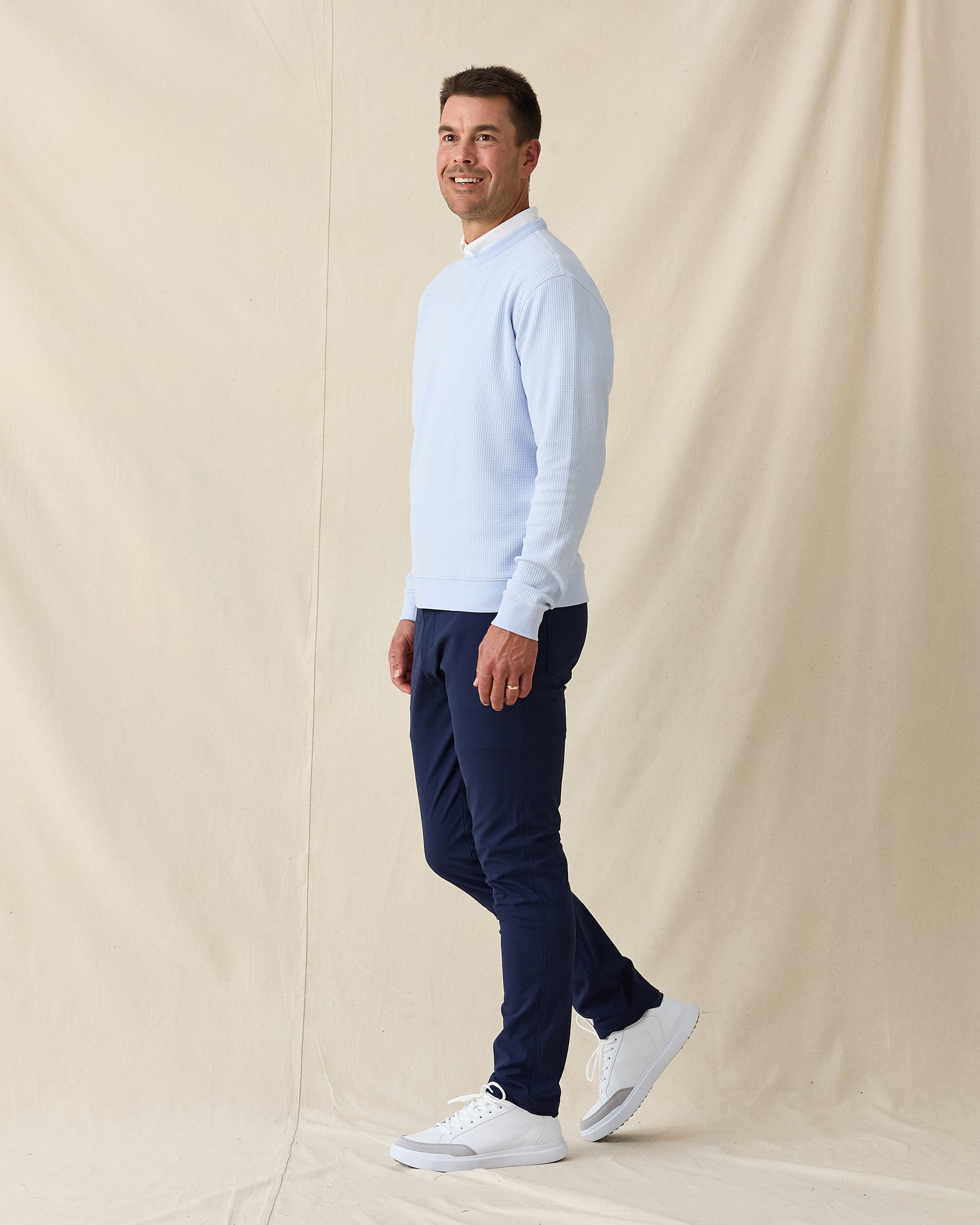 Men’s light blue crewneck pullover styled with navy pants and white sneakers in a clean golf outfit.
