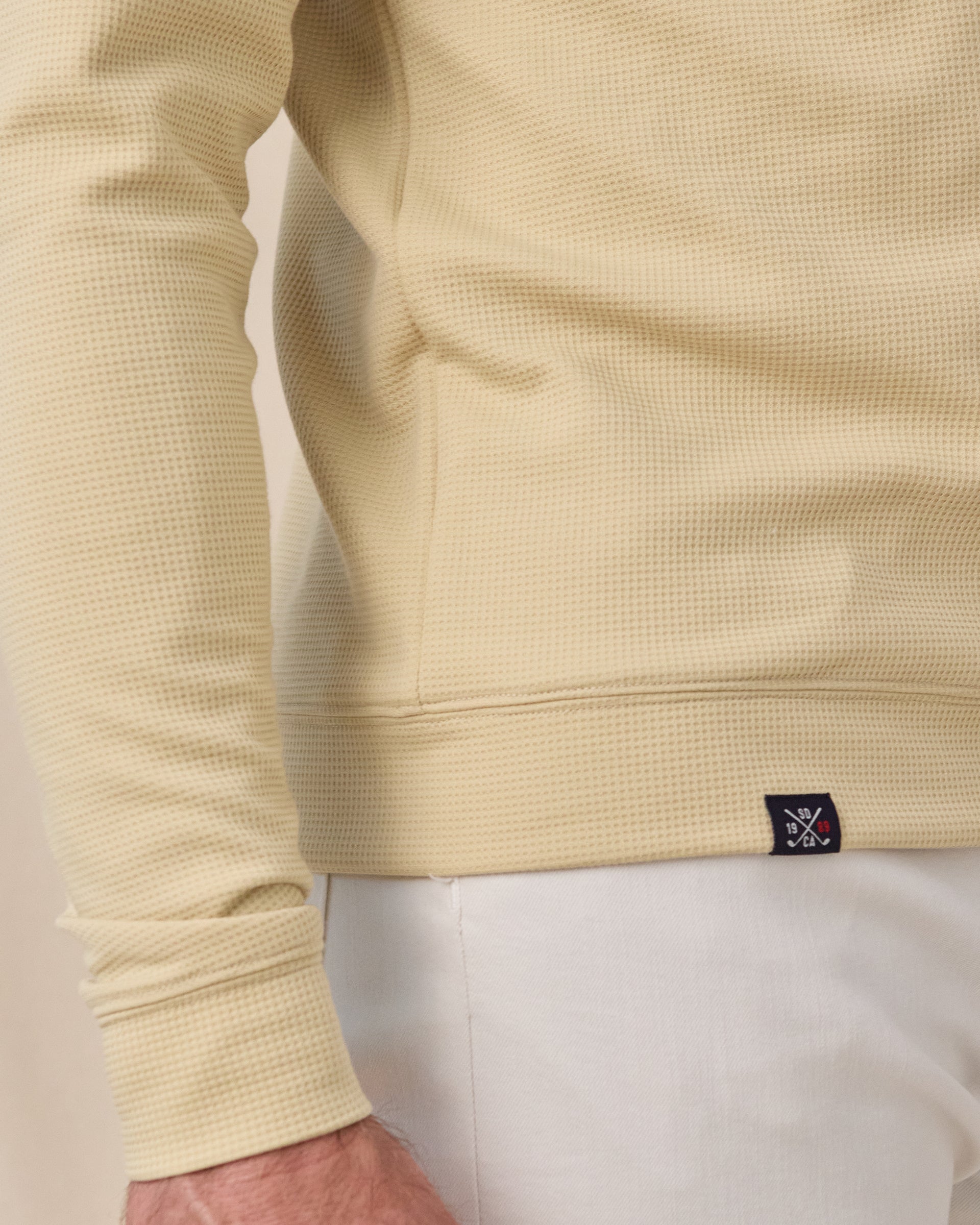 Close-up of the Gridlock Hoodie in Sandstorm showing the waffle knit texture, banded hem, cuff, and woven logo label.