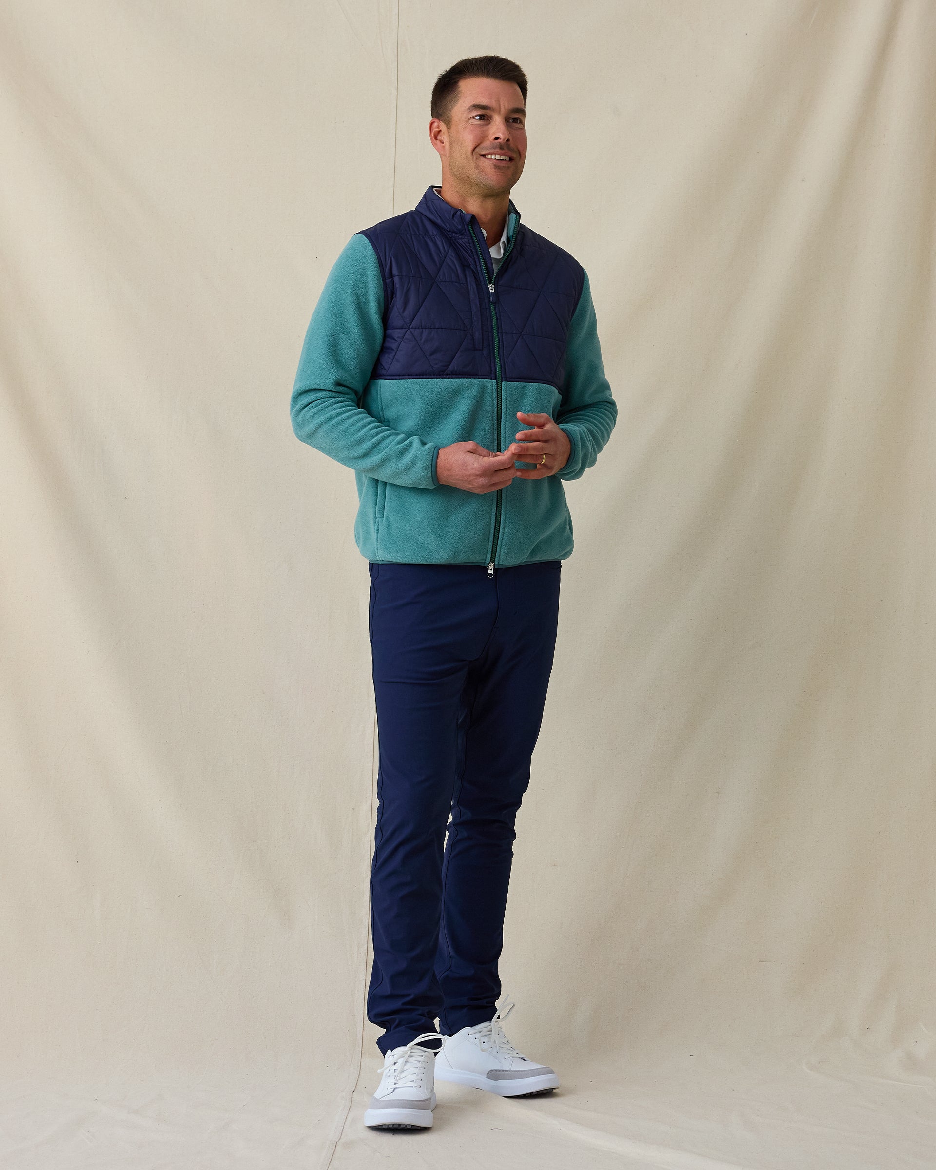 Men's Okemo Hybrid Fleece Jacket in Sage, full length front view on model featuring a navy quilted upper body with a sage fleece lower body and sleeves, paired with navy pants and white shoes