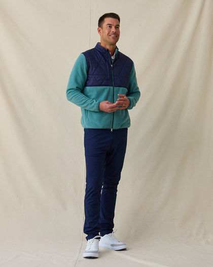 Men's Okemo Hybrid Fleece Jacket in Sage, full length front view on model featuring a navy quilted upper body with a sage fleece lower body and sleeves, paired with navy pants and white shoes