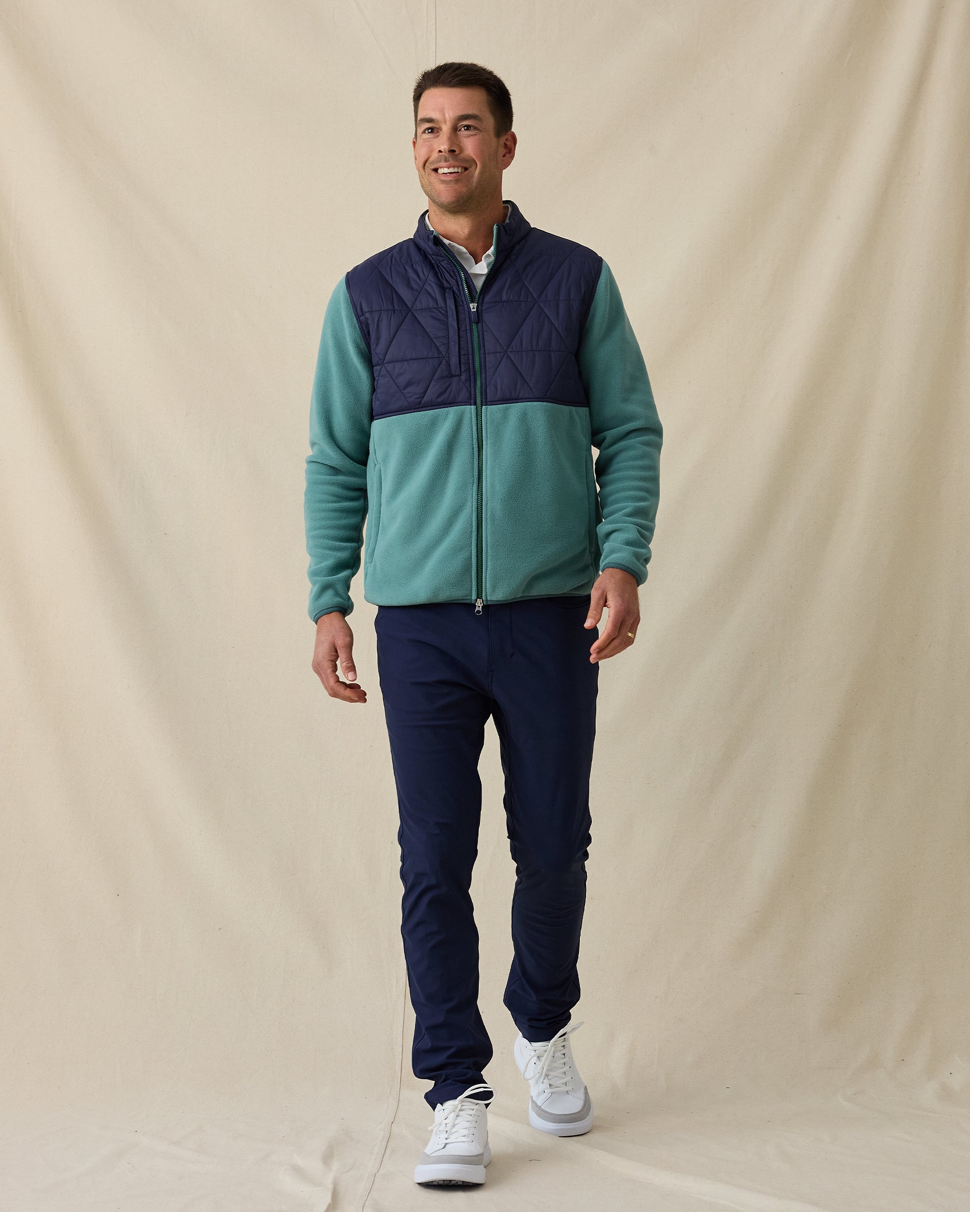 Men's Okemo Hybrid Fleece Jacket in Sage, full length front view on model featuring a navy quilted upper body with a sage fleece lower body and sleeves, paired with navy pants and white shoes