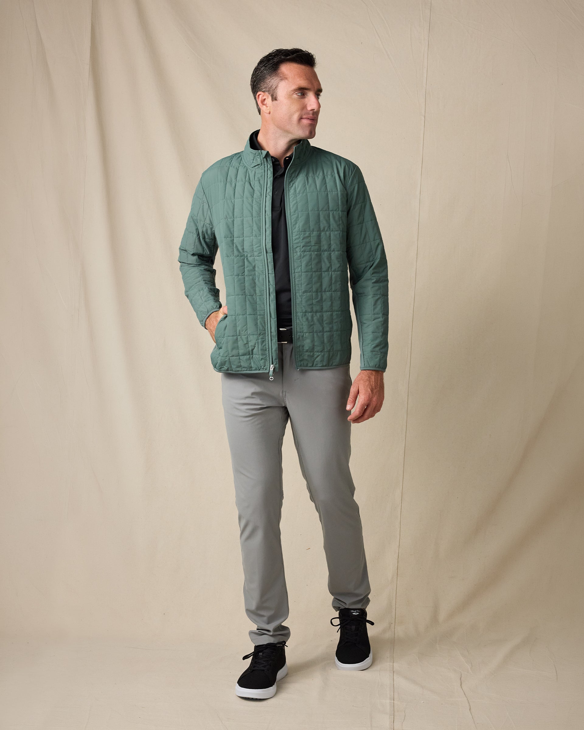 Model wearing the Big Sky Quilted Jacket in Dark Forest with a black polo, gray pants, and black sneakers.