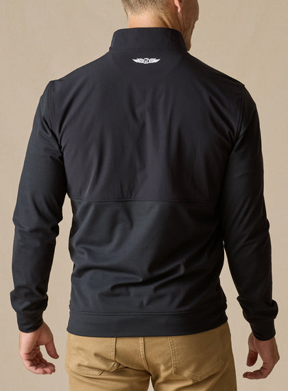 Men's Harding Hybrid Quarter Zip in Black, back view on male model showing white embroidered logo at center back neck and dual-fabric paneling, paired with khaki pants