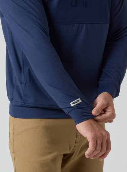 Men's Harding Hybrid Quarter Zip in New Indigo, close-up detail of logo patch at hem and dual-fabric paneling with side pocket