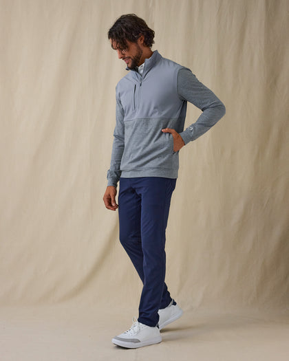 Men's Harding Hybrid Quarter Zip in Storm, full body on model front view featuring a solid steel grey upper body with heathered charcoal grey lower body and sleeves, chest zip pocket and quarter zip detail paired with navy pants and white shoes