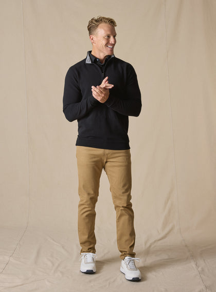 Men's Catalina Quarter Zip in Black, full-length on-model view featuring a black ribbed fabric with a quarter zip closure and gray interior collar, styled with tan pants and white shoes