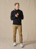 Men's Catalina Quarter Zip in Black, full-length on-model view featuring a black ribbed fabric with a quarter zip closure and gray interior collar, styled with tan pants and white shoes