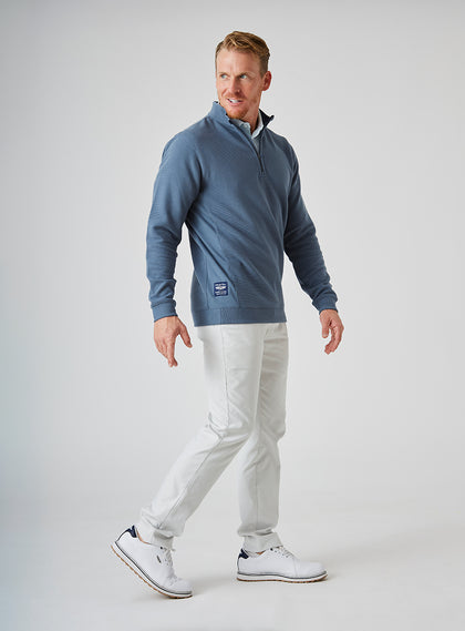Men's Catalina Quarter Zip in Deep Sea, side on-model view featuring a slate blue ribbed fabric with a quarter zip closure and Straight Down woven label at the hem, styled with white pants and white shoes