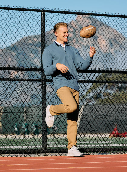 Men's Catalina Quarter Zip in Deep Sea, lifestyle on-model view featuring a model tossing a football outdoors on a track, styled with tan pants and white shoes