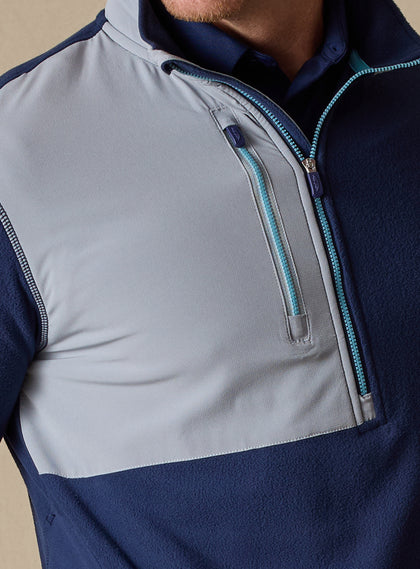 Men's Moonstone Quarter Zip in New Indigo, close-up chest detail featuring gray softshell contrast panel with chest zip pocket, light blue zipper tape, and navy collar with branded zipper pulls
