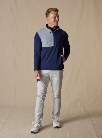 Men's Moonstone Quarter Zip in New Indigo, full-length front model view featuring a navy micro-fleece body with gray contrast chest panel, styled with stone pants and white sneakers against a neutral canvas backdrop