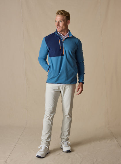 Men's Moonstone Quarter Zip in Petrol, full-length front model view featuring a medium blue micro-fleece body with navy contrast chest panel, styled with stone pants and white shoes against a neutral canvas backdrop