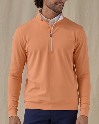 Men's Patron Quarter Zip in Citrus, front view on model featuring a solid peach orange body with a quarter zip neckline, paired with navy pants