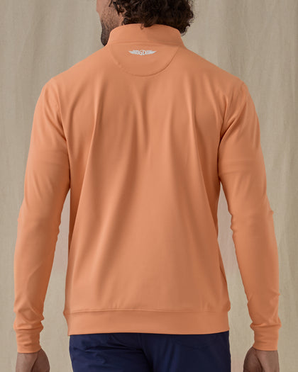 Men's Patron Quarter Zip in Citrus, back view on model featuring a solid peach orange body with a Straight Down logo embroidered at the upper back, paired with navy pants