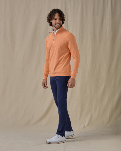 Men's Patron Quarter Zip in Citrus, full-length front view on model featuring a solid peach orange body with a quarter zip neckline, paired with navy pants and white shoes