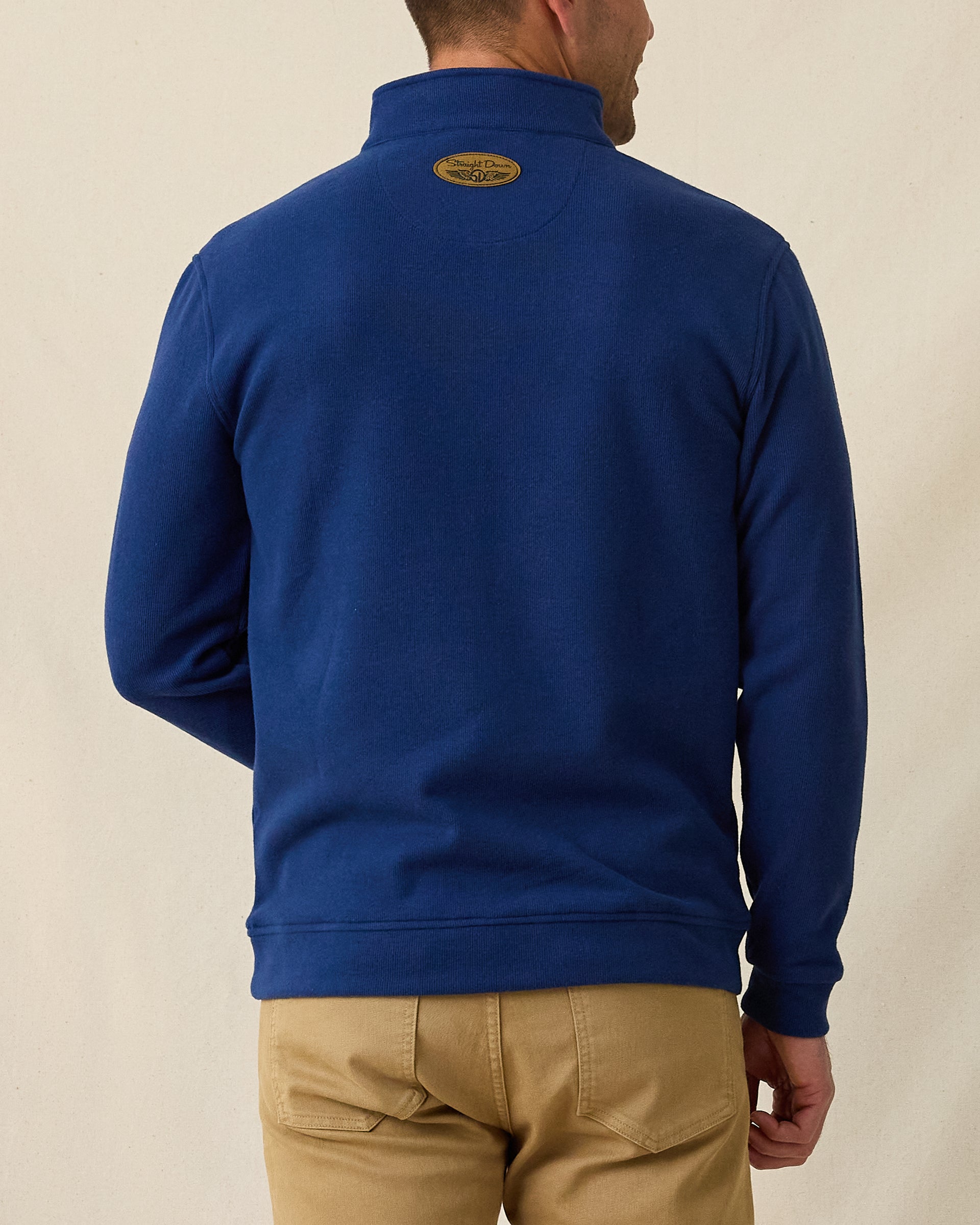 Men's Montecito Quarter Zip in New Indigo, back view on model featuring a ribbed knit texture with tan Straight Down leather patch at center back neck, layered over a white polo, paired with khaki pants