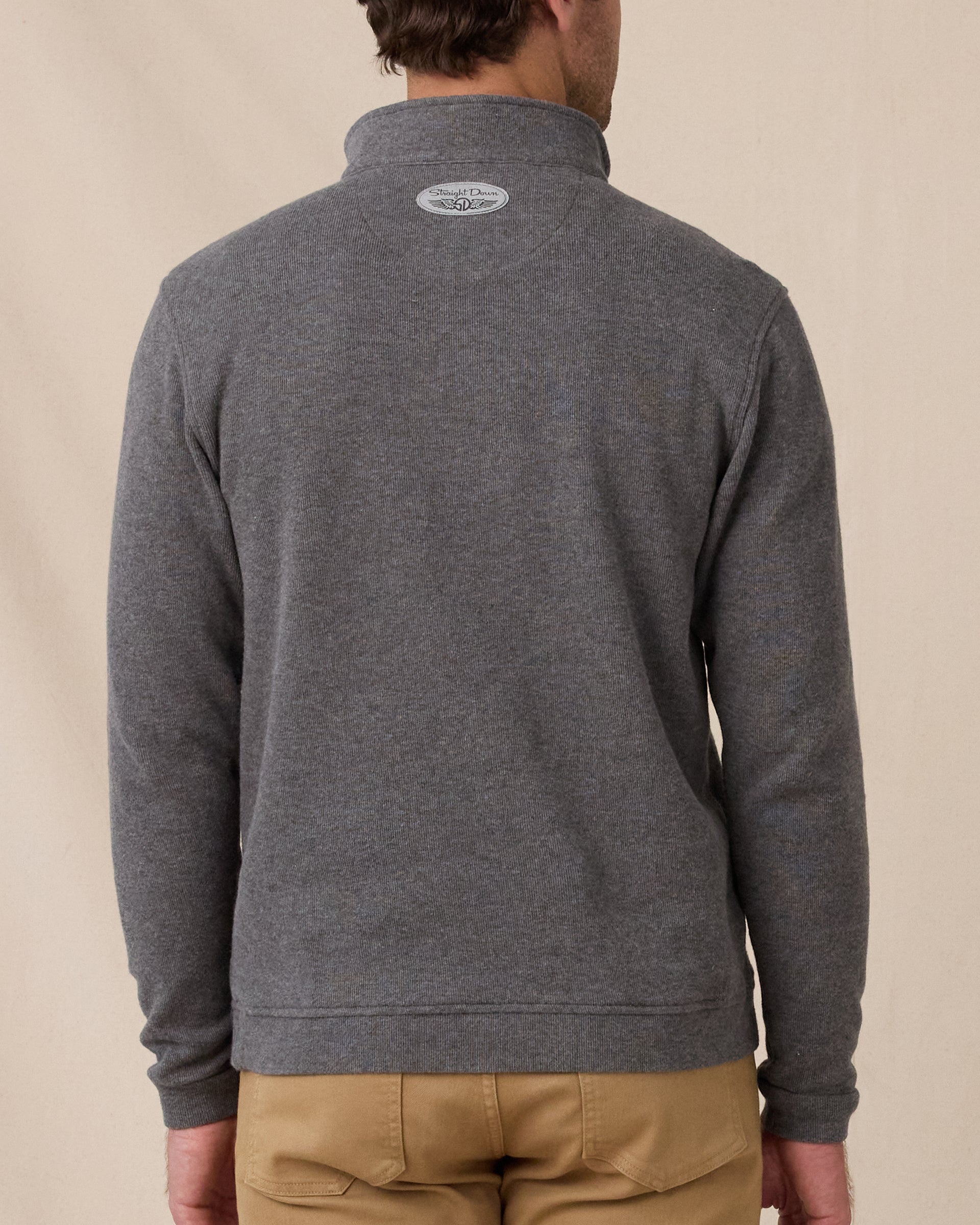 A model viewed from the back wearing a dark heather gray quarter-zip pullover sweater and tan pants, against a plain beige studio background.