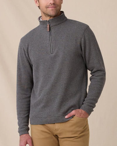 A model wearing a dark gray heathered quarter-zip pullover sweater with a brown leather zipper pull, paired with tan pants, against a neutral beige background.