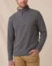 A model wearing a dark gray heathered quarter-zip pullover sweater with a brown leather zipper pull, paired with tan pants, against a neutral beige background.