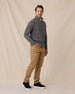 A man modeling a gray quarter-zip pullover sweater, tan pants, and black sneakers against a beige fabric backdrop.