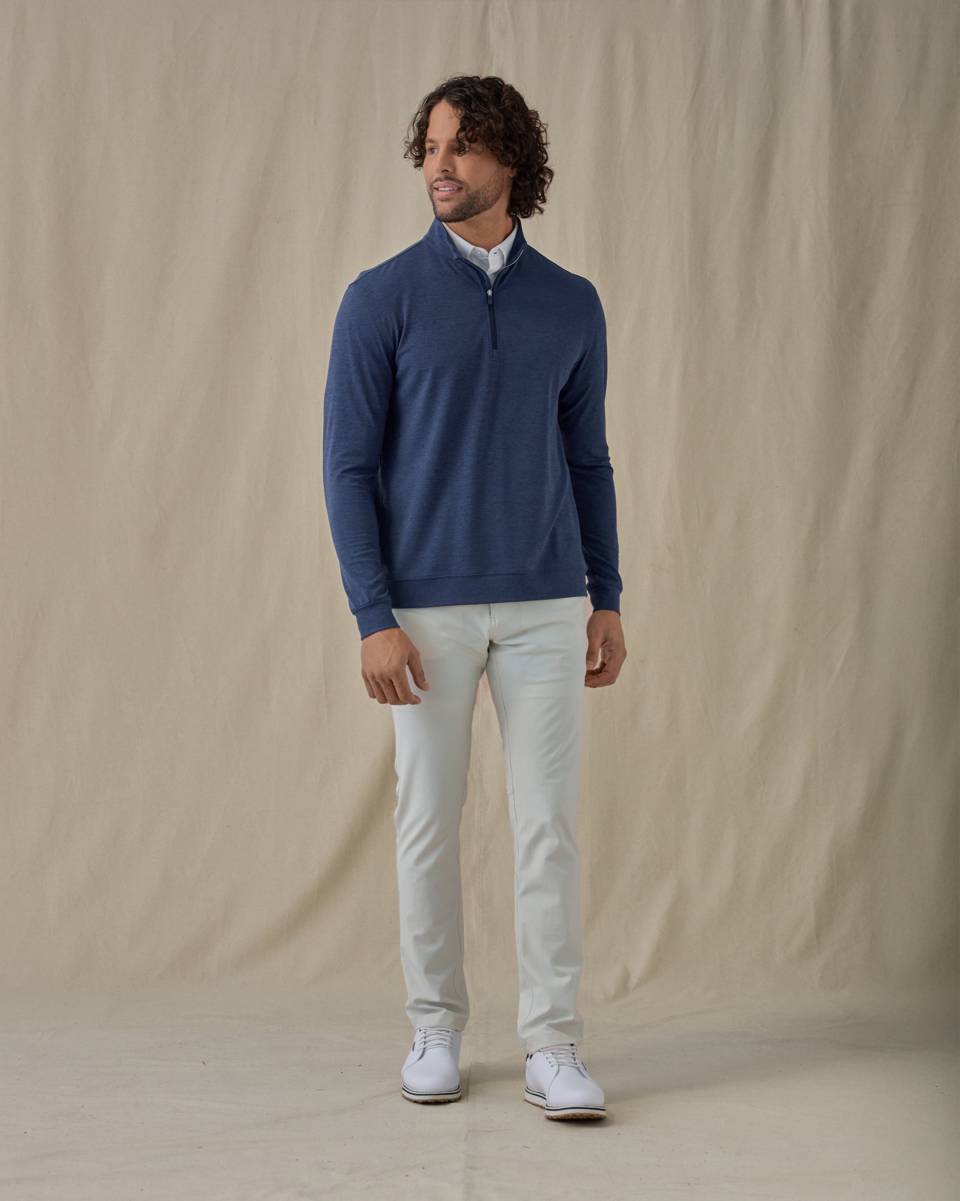 Men's Tiburon Quarter Zip in New Indigo, full-length front view on model featuring a solid heathered navy body with a quarter zip neckline, layered over a white polo, paired with light gray pants and white shoes