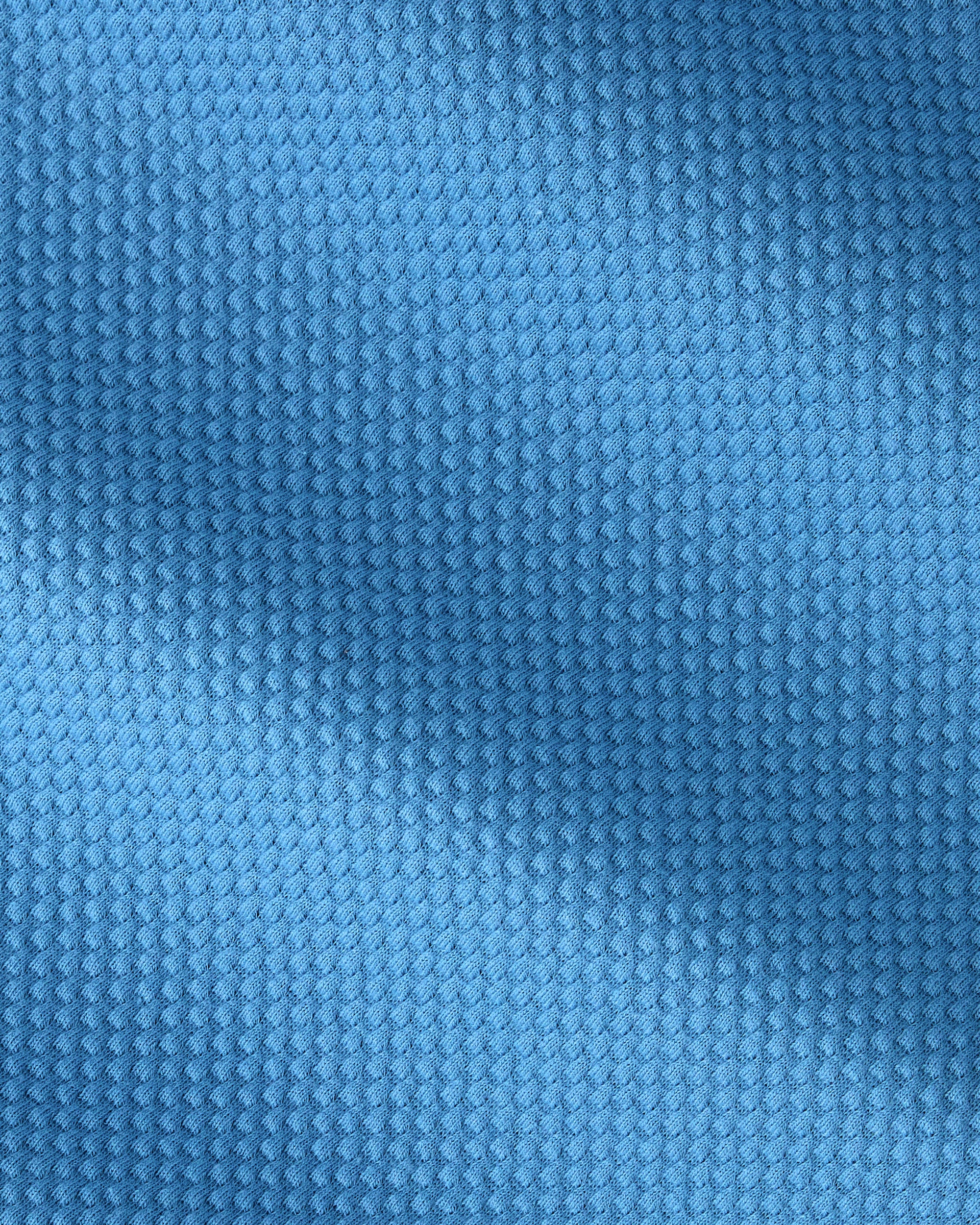 A close-up of a textured blue fabric with a fine, repeating waffle or mesh-like pattern.