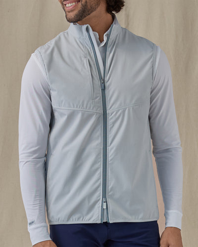 Men's Zephyr Hybrid Vest in Silver, front view on model featuring a solid light gray body with a full zip closure and mock neck, layered over a white polo and long sleeve, paired with navy pants