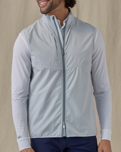 Men's Zephyr Hybrid Vest in Silver, front view on model featuring a solid light gray body with a full zip closure and mock neck, layered over a white polo and long sleeve, paired with navy pants