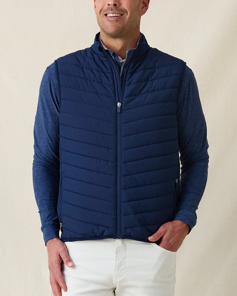 Men's Delta 2.0 Quilted Hybrid Vest in New Indigo, front view on model featuring a navy quilted front panel with full zip closure, layered over a navy long sleeve shirt, paired with white pants