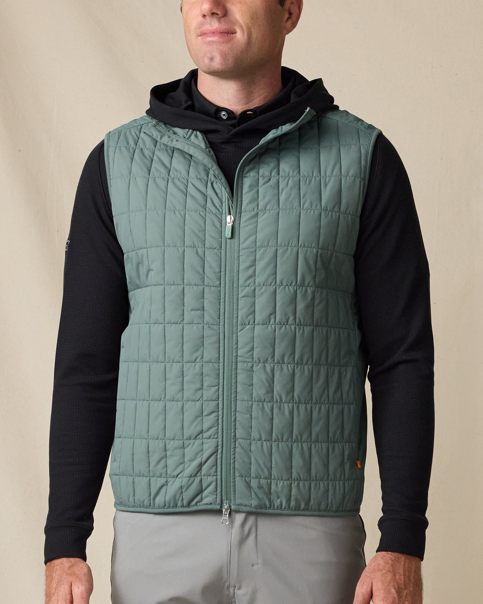 Model wearing the Big Horn Vest in Dark Forest, featuring grid quilting, a full-zip front, and layered over a black hoodie.