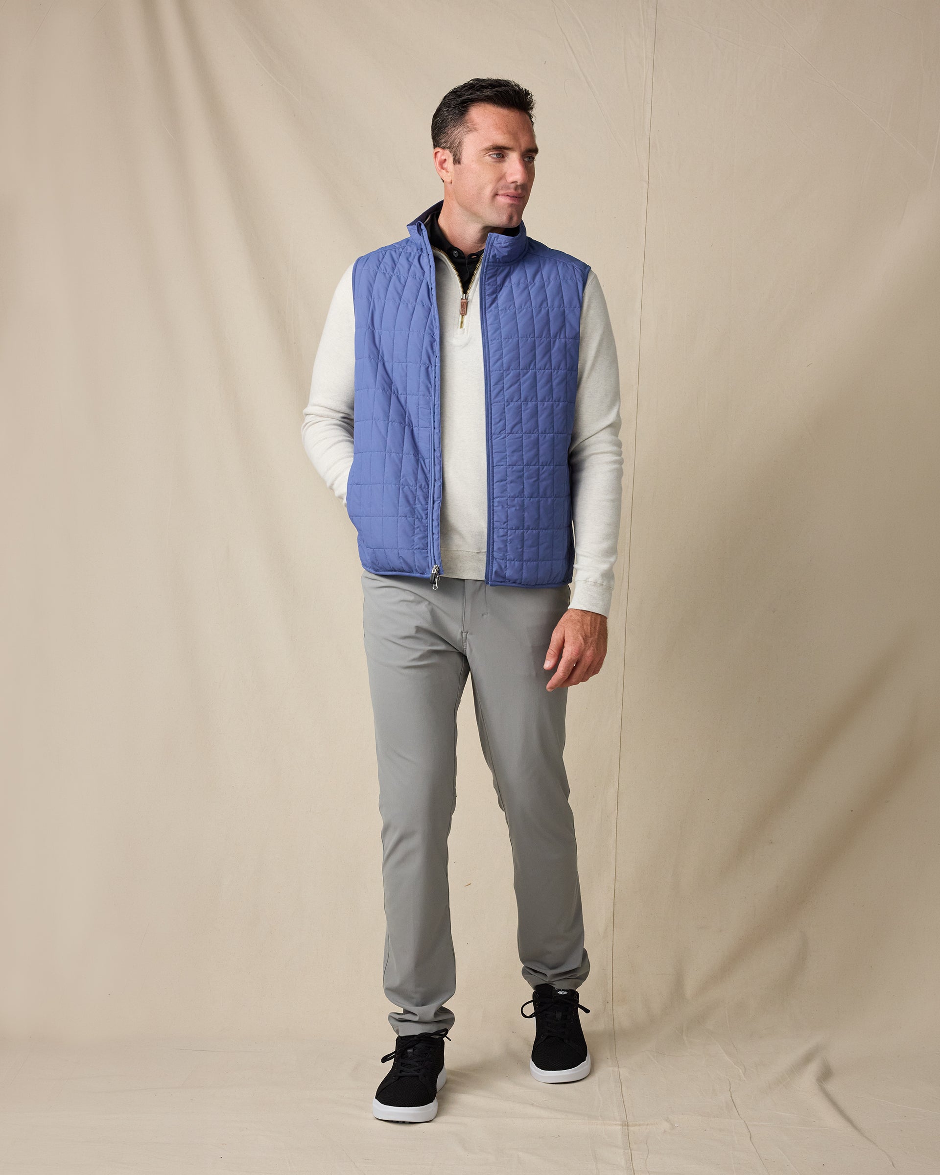 Model wearing the Big Horn Vest in Moonlight layered over a light quarter zip with gray pants and black sneakers.