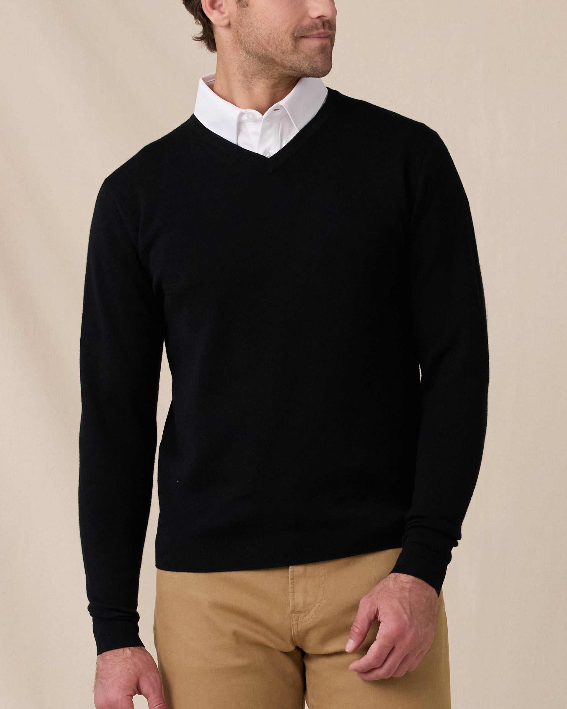 Man wearing the black Connery V-Neck Sweater layered over a white collared shirt with tan pants.