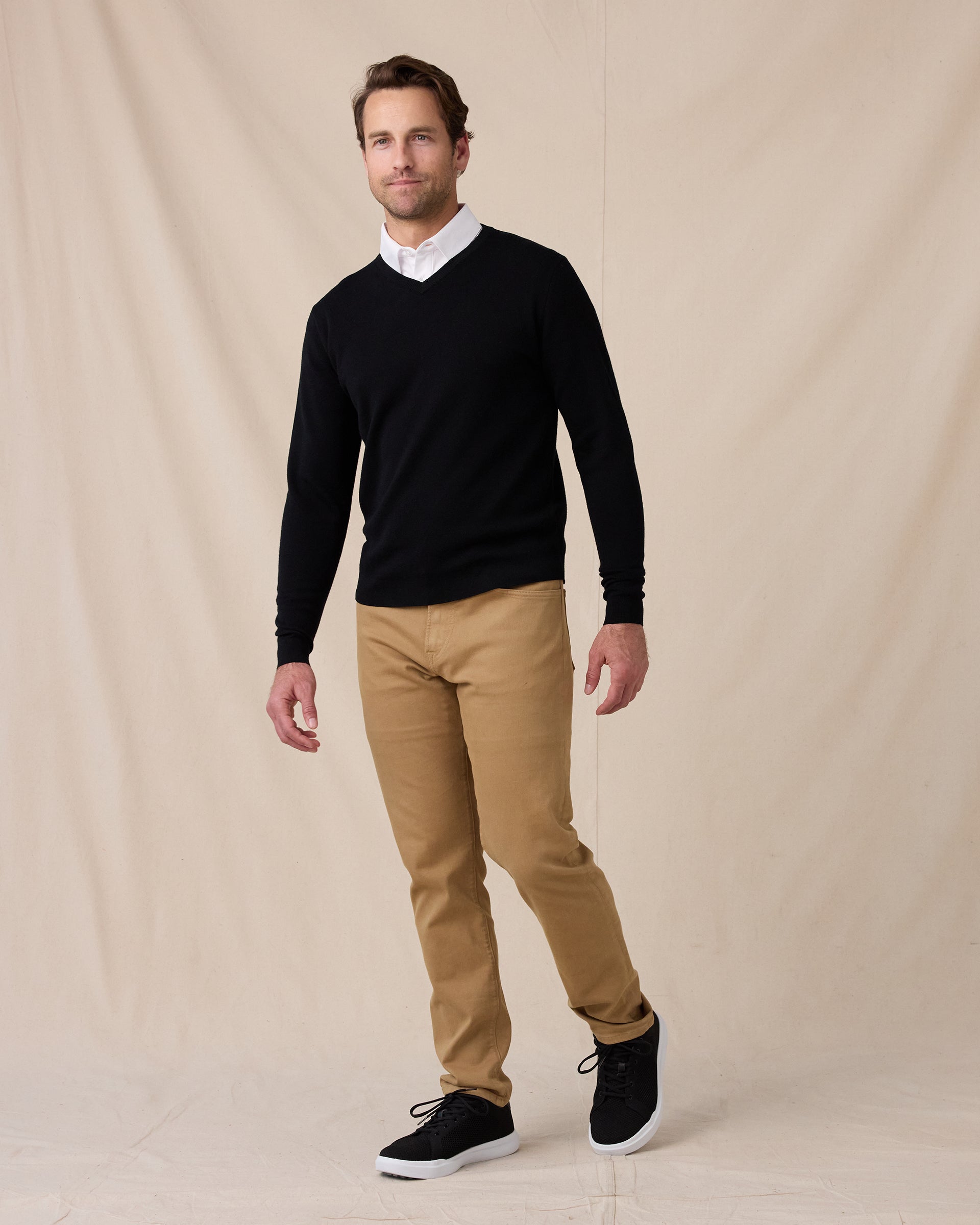 Man wearing the black Connery V-Neck Sweater over a white collared shirt, paired with tan pants and black sneakers.