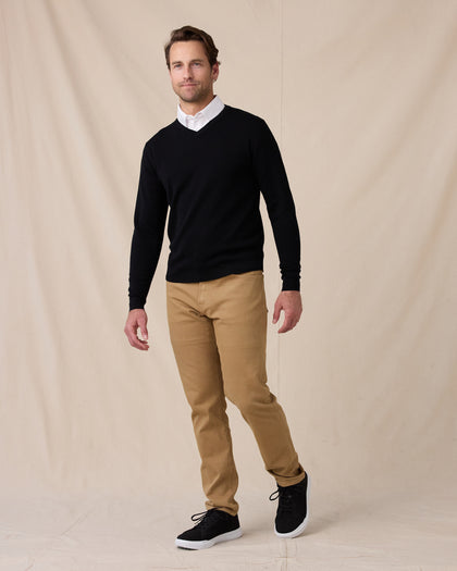 Man wearing the black Connery V-Neck Sweater over a white collared shirt, paired with tan pants and black sneakers.
