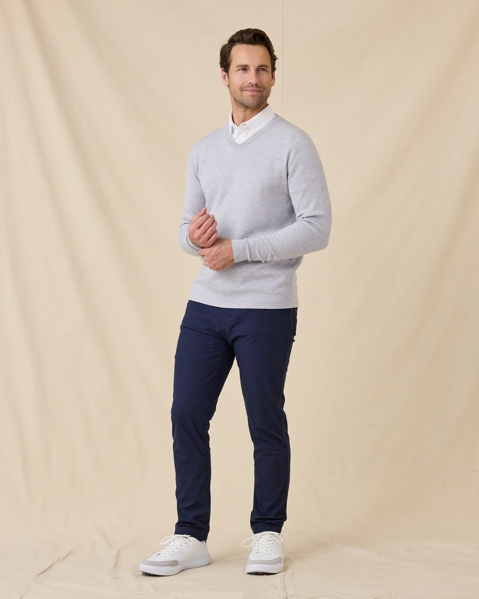 Man wearing the Light Grey Connery V-Neck Sweater over a white collared shirt, paired with navy pants and white sneakers.
