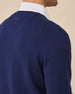 Close-up back view of a model wearing a navy blue knit sweater over a white collared shirt, against a plain beige background.