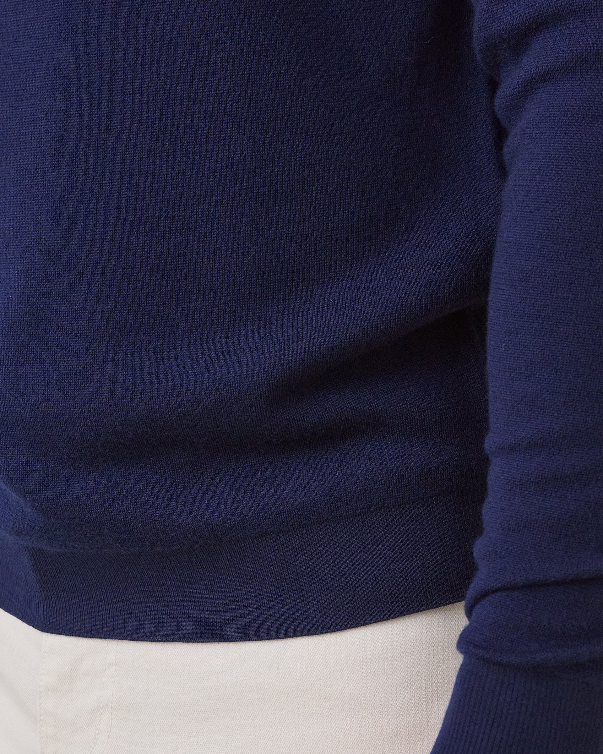 Close-up of a navy blue knit sweater worn with white pants, showing the ribbed hem and sleeve cuff.