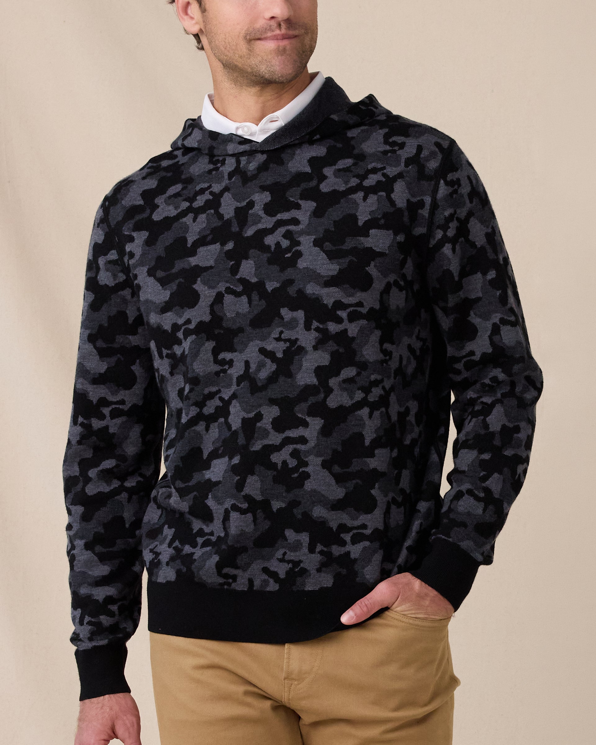 Model wearing the Crenshaw Reversible Sweater Hoodie in Charcoal over a white polo, showing the camouflage pattern and hooded design.