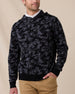 Model wearing the Crenshaw Reversible Sweater Hoodie in Charcoal over a white polo, showing the camouflage pattern and hooded design.
