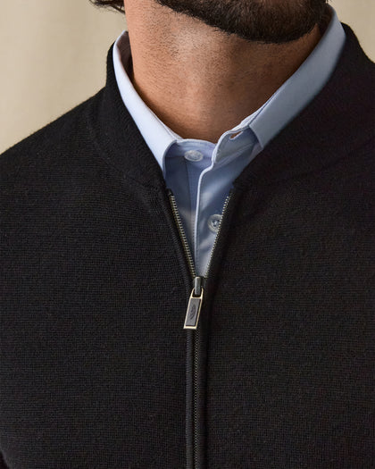 Men's Sarazen Knit Bomber in Black, on model front close-up view featuring fine knit texture detail, stand collar, and Straight Down branded gunmetal zipper pull worn over a light blue polo