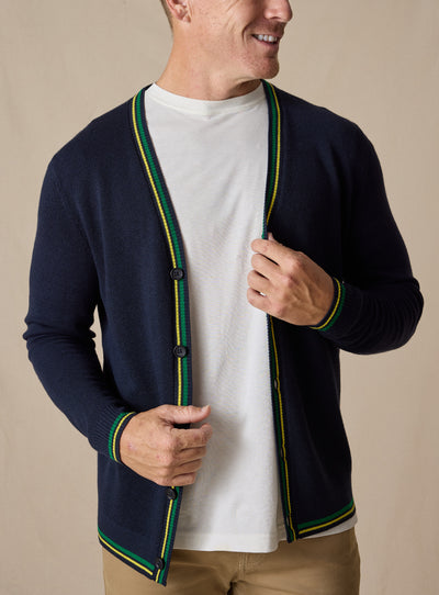 Men's Gilmore Cardigan in New Indigo, front view featuring a navy knit body with green and yellow tipped trim, paired with a white t-shirt and khaki pants