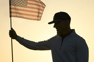 Golfer holding flag stick with an American flag at sunset, wide banner image