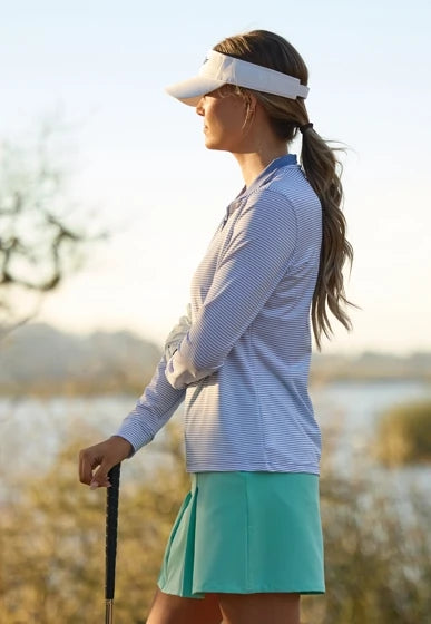 Women’s golfer wearing the Kiri Stripe Quarter Zip and cascade green Korra skort on the golf course