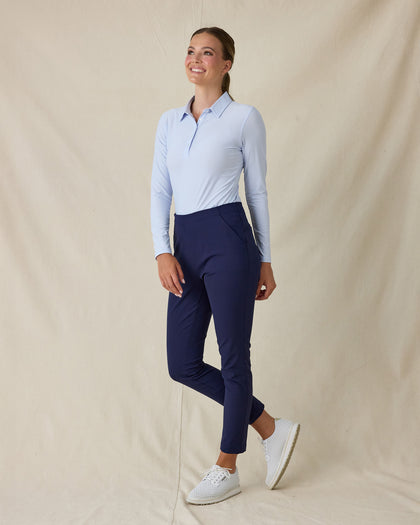 Women's Midday Long Sleeve Polo in Powder, full length side angle view on model featuring a light blue long sleeve polo with a spread collar, paired with navy pants and white golf shoes